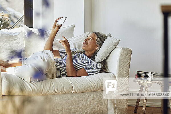 Frau  die ein Mobiltelefon benutzt  während sie auf dem Sofa im Wohnzimmer liegt