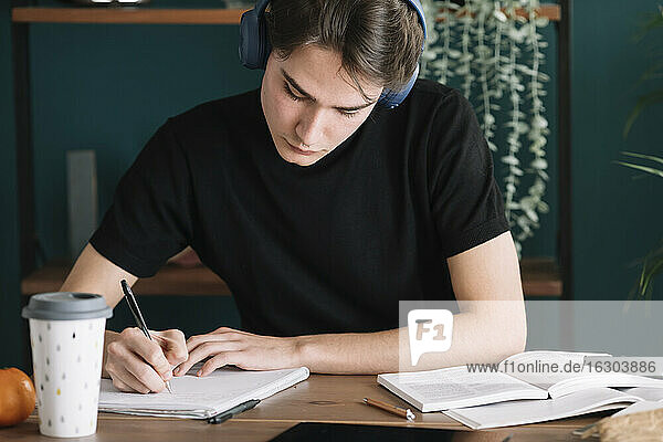 Mann schreibt in ein Buch  während er zu Hause über Kopfhörer Musik hört