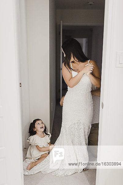 Smiling daughter looking at mother getting dressed for wedding