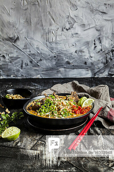 Schale mit roter Currysuppe mit Reisnudeln  Rindfleisch  Gemüse  Frühlingszwiebeln  Erdnüssen und Limette