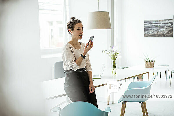 Geschäftsfrau  die ein Mobiltelefon benutzt  während sie am Tisch steht