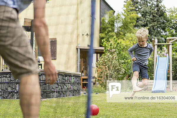 Blonder Junge  der beim Fußballspielen mit seinem Vater im Hinterhof einen Ball tritt