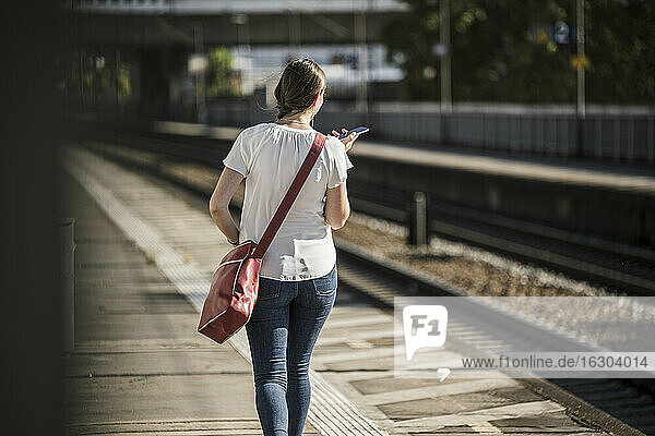 Woman using mobile phone while walking on railroad station platform