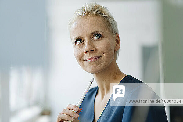 Nahaufnahme einer Geschäftsfrau  die im Büro einen digitalisierten Stift hält und wegschaut