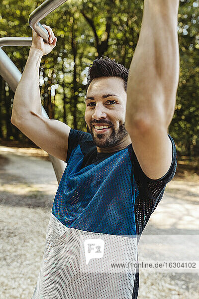 Porträt eines lächelnden Mannes  der sich auf einem Fitnessparcours aufrichtet