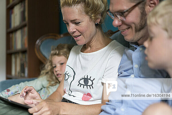 Frau teilt digitales Tablet mit Familie im heimischen Wohnzimmer