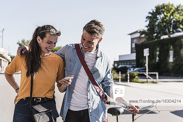 Happy young woman showing smartphone to boyfriend while walking in city