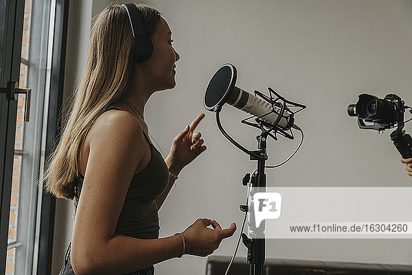 Teenager-Mädchen mit Kopfhörern singt über Mikrofon im Studio