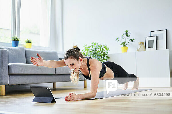 Frau streckt den Arm während der Plank-Pose aus  während sie im Internet über einen Tablet-PC eine Übung lernt