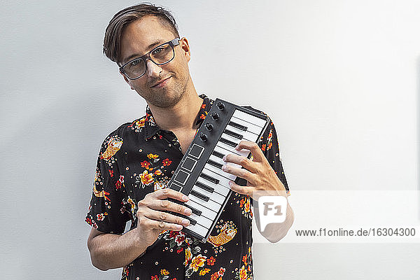Smiling man holding midi keyboard while standing against wall
