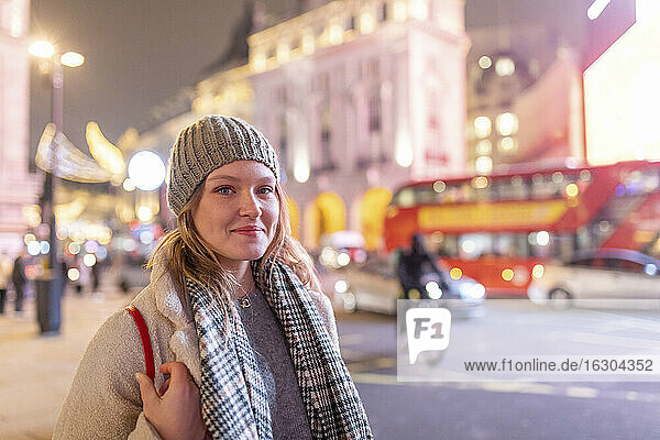 Young woman wearing warm clothing standing in Piccadilly Circus at night