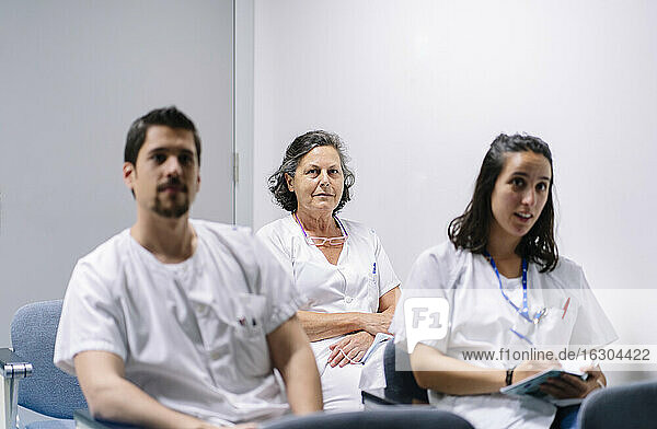 Ärzte hören in einer Sitzung zu  während sie im Krankenhaus an der Wand sitzen