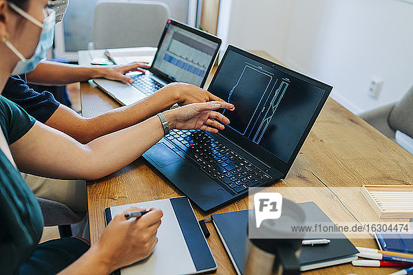 Programmierer diskutieren über Laptop  während sie im Büro während des Coronavirus einen Mundschutz tragen