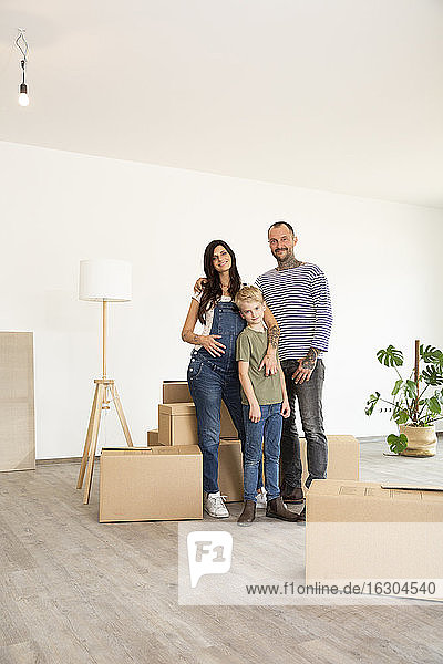 Happy family standing by cardboard boxes against wall in new home