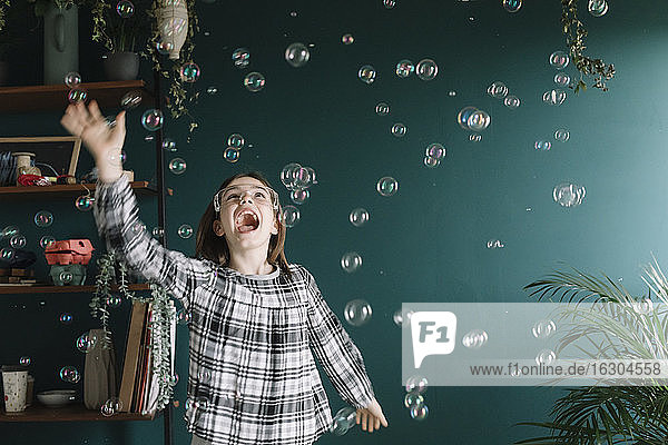 Mädchen spielt mit Seifenblasen  während sie zu Hause an der Wand steht