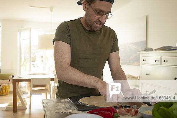 Mann bereitet Pizza zu  während er über der Kücheninsel Lebensmittel zerkleinert