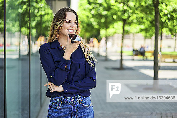 Smiling woman looking away using speaker while talking through smart phone