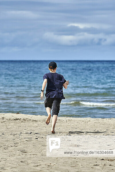 Junge läuft am Strand während eines sonnigen Tages gegen den Himmel