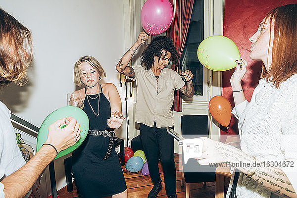Freunde tanzen mit Luftballons während einer Party zu Hause