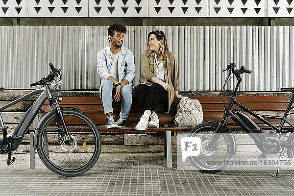 Couple sitting on bench while electric bicycles parked on footpath