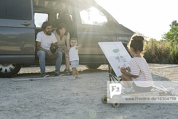 Mädchen malt  während die Eltern im Van mit der kleinen Schwester im Park bei Sonnenuntergang sind