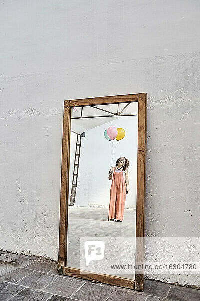 Reflexion der Frau hält bunte Heliumballons auf Spiegel gegen weiße Wand