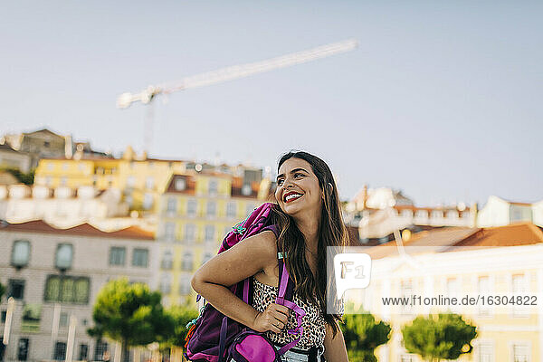 Smiling young woman with backpack looking away while standing in city