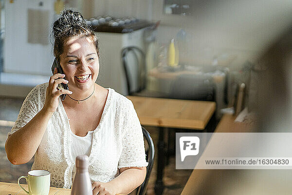 Fröhliche  üppige Frau  die in einem Café sitzt und über ein Mobiltelefon spricht
