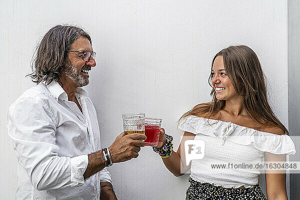 Smiling man toasting drinks with daughter while standing against wall