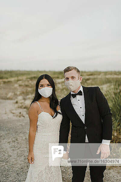 Bride and groom with protective face mask in field during COVID-19