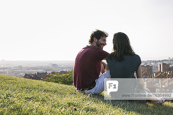 Lächelnder Mann  der eine Frau ansieht  während er im Gras vor einem klaren Himmel sitzt