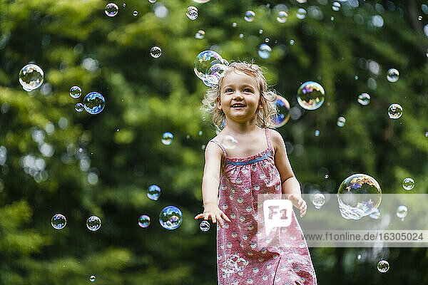 Glückliches Mädchen genießt beim Laufen inmitten von Seifenblasen im Park