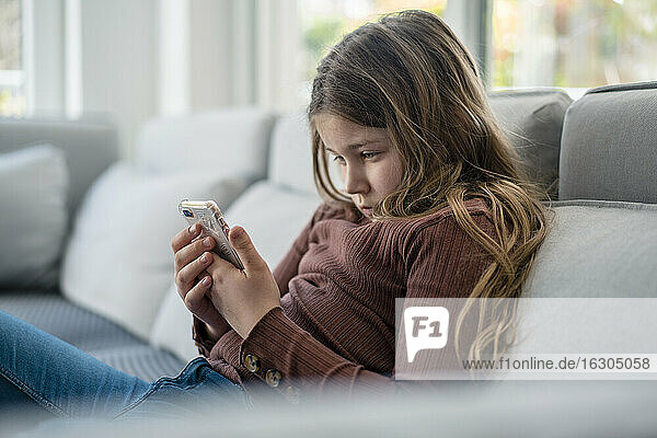 Mädchen benutzt ihr Smartphone auf dem Sofa sitzend