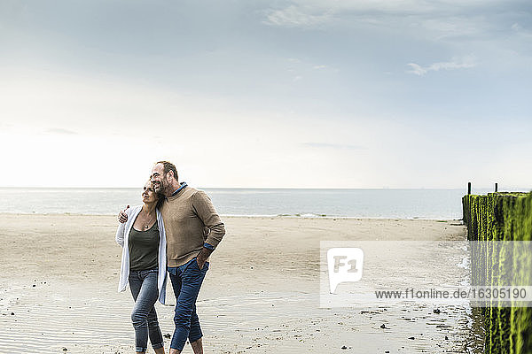 Loving mature couple walking at beach against sea during sunset