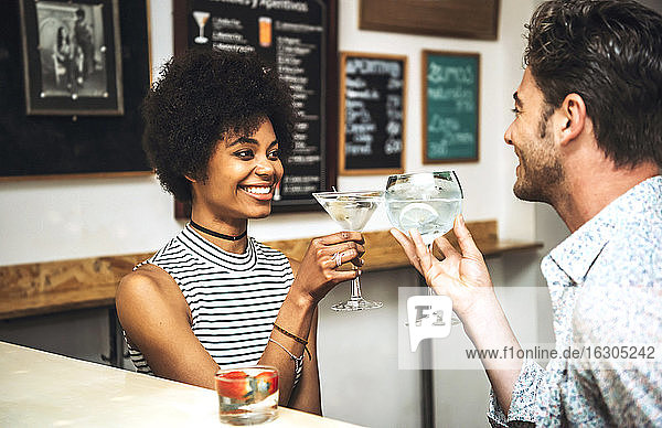 Glückliches Paar stößt mit Getränken an  während es an der Bar sitzt
