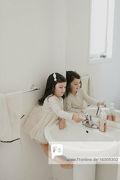 Mädchen wäscht die Hand und balanciert zwischen Wand und Waschbecken im Badezimmer