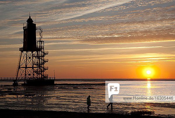 Germany  Lower Saxony  Dorum  lighthouse Obereversand and two walkers at sunset