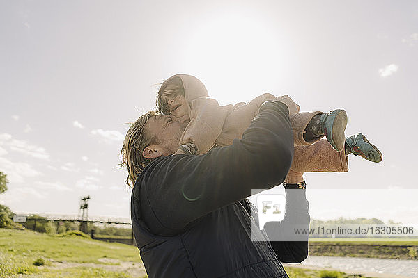 Fröhlicher Vater kuschelt mit seiner Tochter und hebt sie an einem sonnigen Tag in die Luft