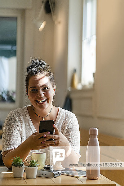 Cheerful voluptuous woman using mobile phone while sitting at table in coffee shop
