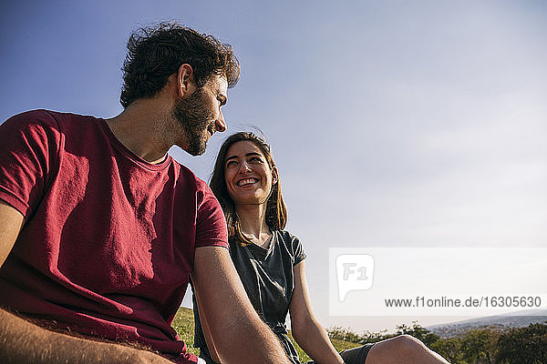 Couple looking at each other while sitting against clear sky