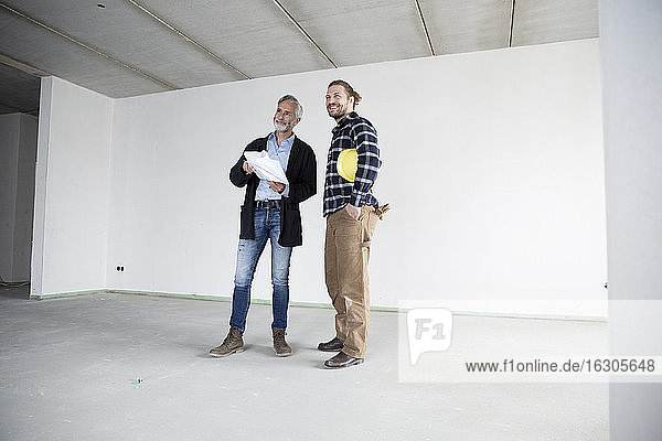Architekt und Bauarbeiter schauen weg  während sie in einem leeren Haus an der Wand stehen