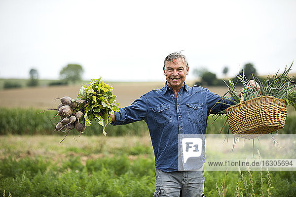 Ein Mann lächelt  während er auf einem Bauernhof Gemüse in beiden Händen hält