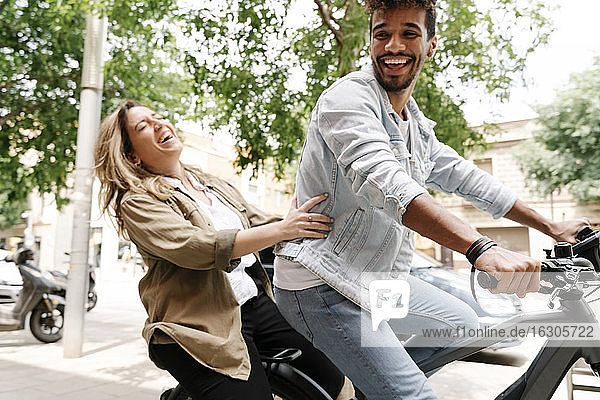Fröhliches junges Paar genießt Fahrt auf elektrischem Fahrrad in der Stadt