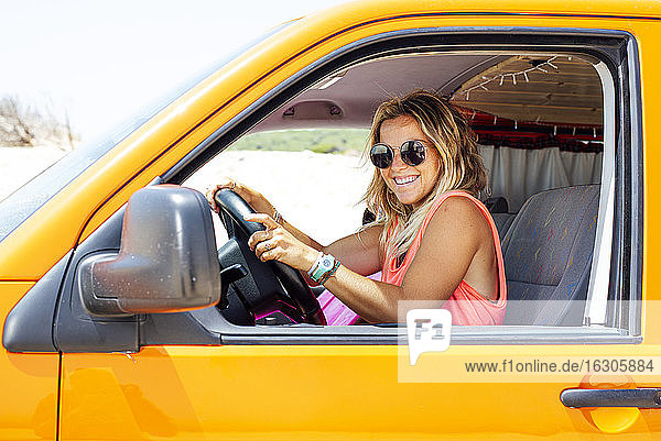 Lächelnde blonde Frau  die in einem Lieferwagen sitzt und die Hände auf das Lenkrad legt
