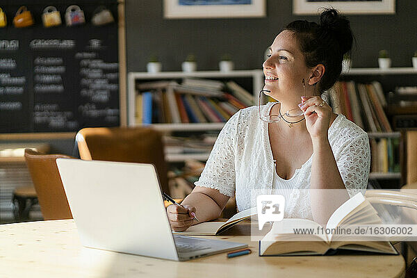 Voluptuous woman with books and laptop on table contemplating while sitting in cafe
