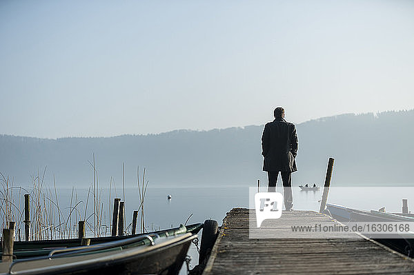 Man standing on wooden boardwalk watching at lake