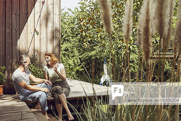 Fröhliches Paar unterhält sich  während es vor einem kleinen Haus im Hof sitzt