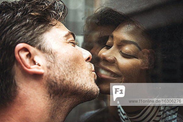 Nahaufnahme eines romantischen Mannes  der seine Freundin durch ein Glasfenster küsst