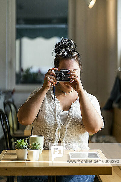 Junge Frau beim Fotografieren mit der Kamera  während sie am Tisch in einem Café sitzt