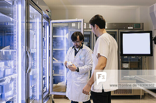 Male pharmacists taking inventory while standing by illuminated refrigerator in hospital